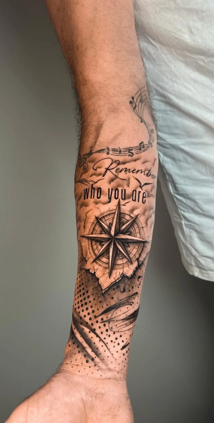 Realism compass rose on torn parchment with the words Remember who you are and music notes, on the forearm.