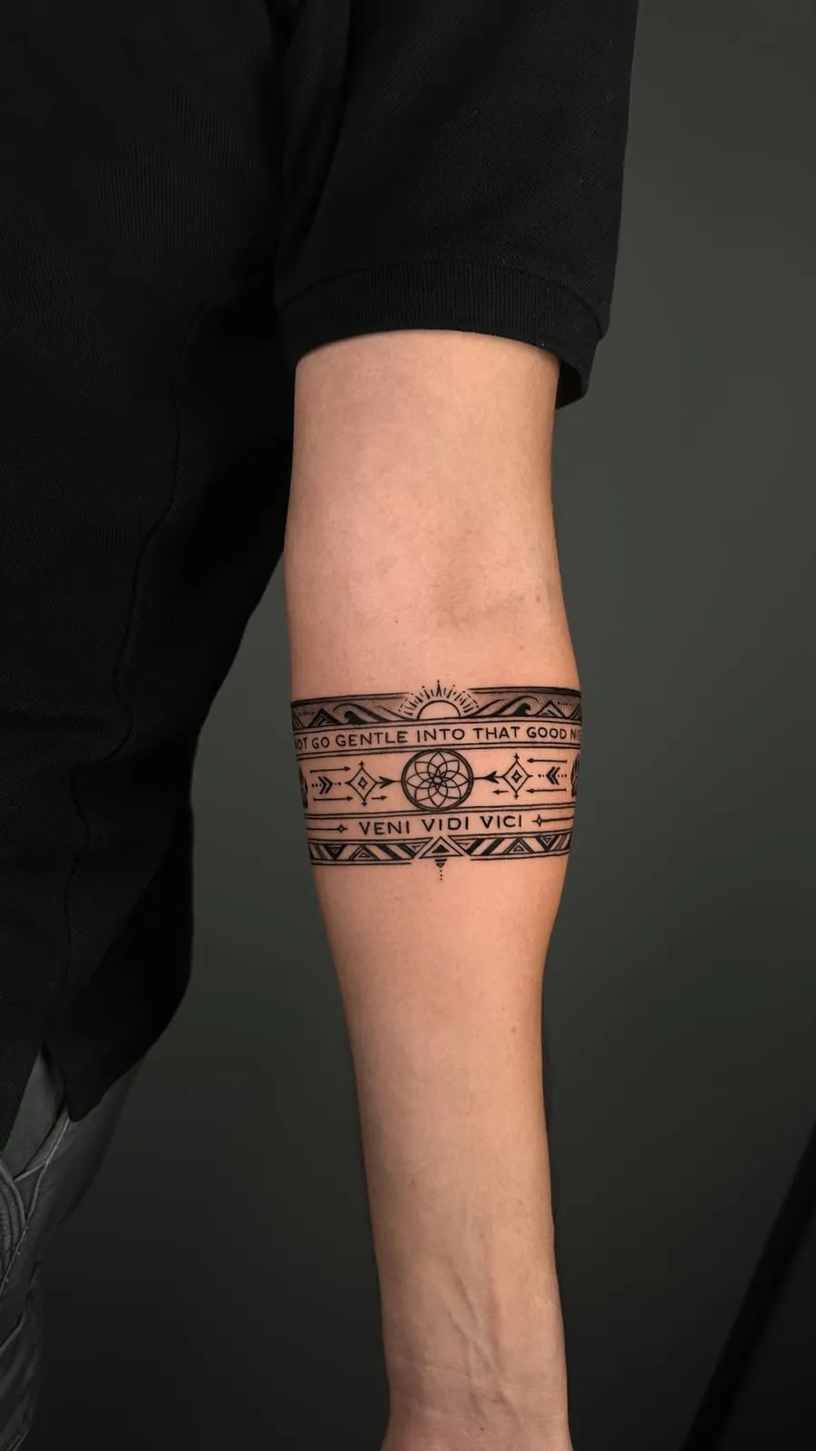 Ornamental armband with 'Do not go gentle into that good night' and 'Veni vidi vici', on the forearm.