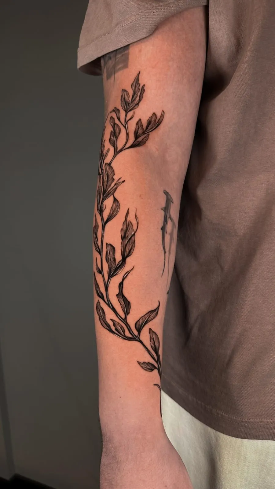 Fine-line vine of shaded leaves winding along the forearm.