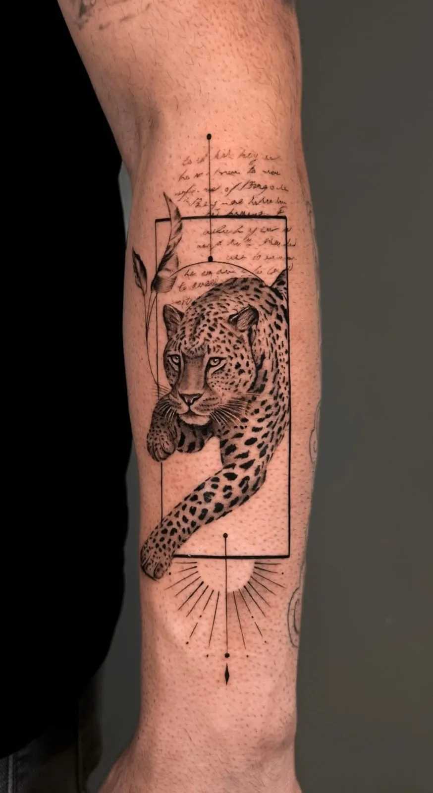 Realism leopard stepping out of a fine-line rectangular frame with handwriting and a small sun, on the forearm.