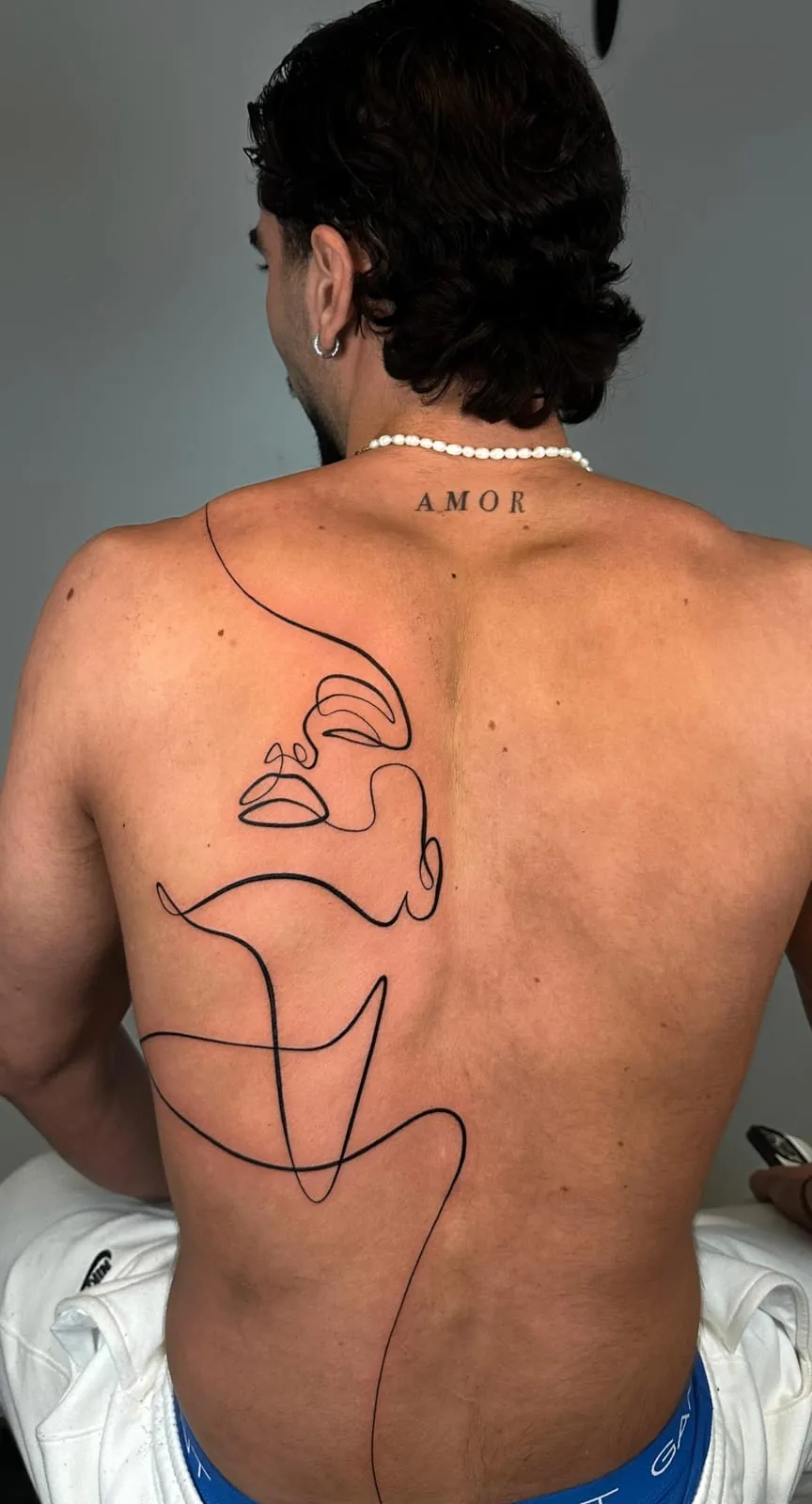 Large single-line drawing of a face and body across the back, under 'Amor' at the neck.