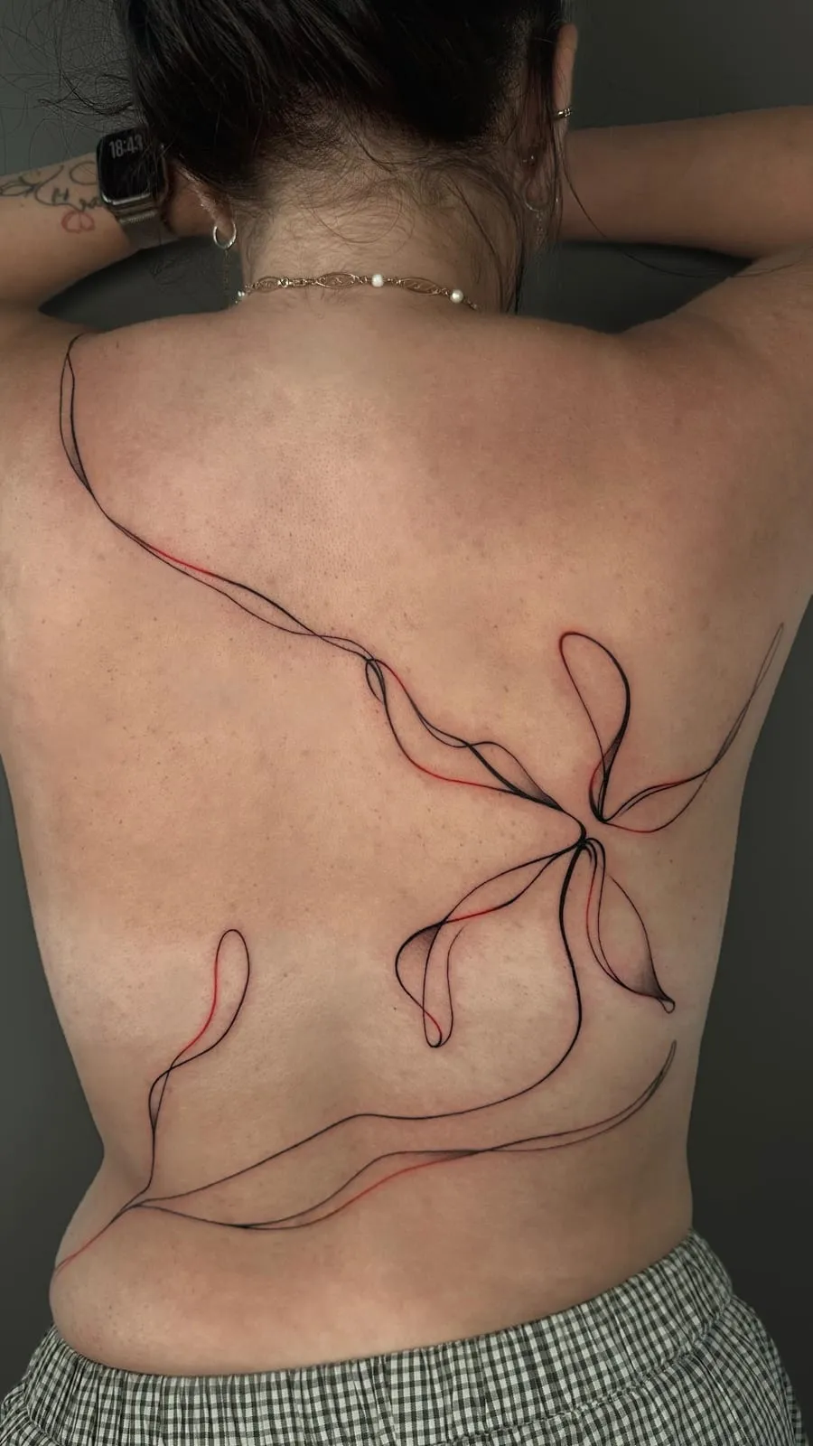 A long ribbon tied in a bow, in black and red fine line, flowing across the back.
