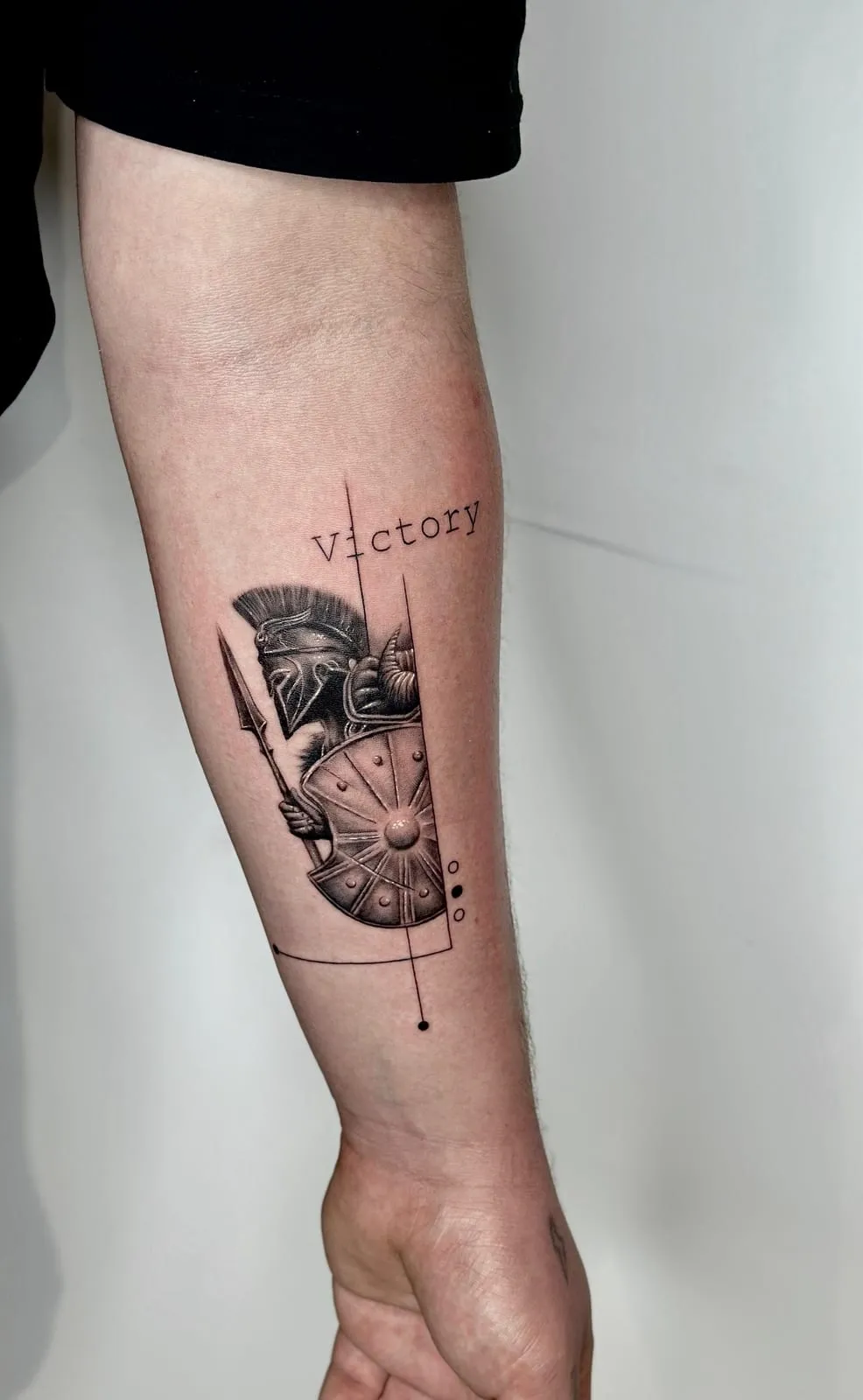 Spartan helmet, spear and shield in black and grey, with fine lines and the word Victory, on the forearm.