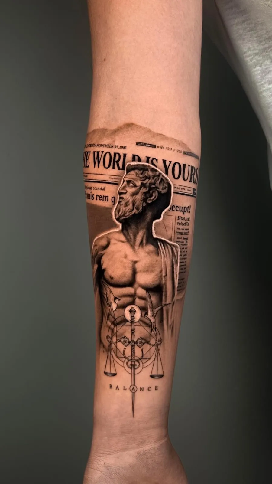 Realism tattoo of a classical statue bust over a newspaper headline reading The World Is Yours, with scales and a sword, on the forearm.